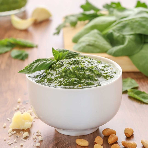 white bowl holding spinach basil pesto, garnished with a basil leaf and with spinach and more pesto