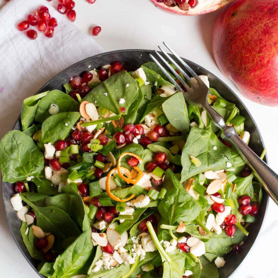 A baby spinach salad topped with sliced almonds, pomegranate arils, and a clementine vinaigrette.