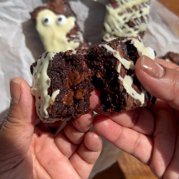 hands breaking in half to show mid section of one rectangular slice of chocolate brownie, that has b