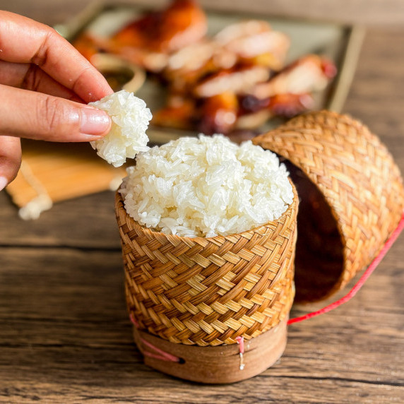 Thai sticky rice in a bamboo basket, with grilled chicken in the background.