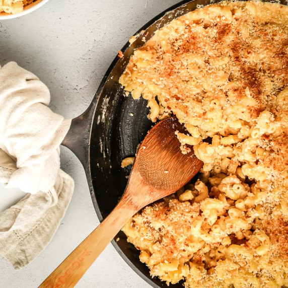 Overhead close up shot of Mac and cheese in a skillet with a portion taken out with a wooden spoon. 