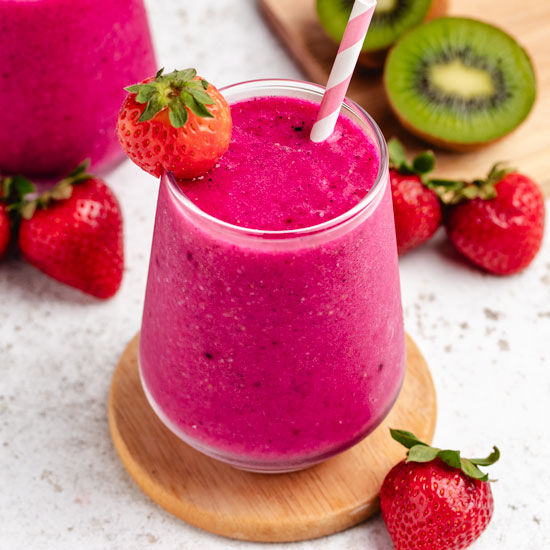 Dragon fruit strawberry smoothie in a glass with a strawberry and a straw.