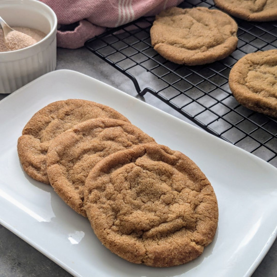 Three sugar and spice cookies on a plate with additional cookies on a wire rack behind.