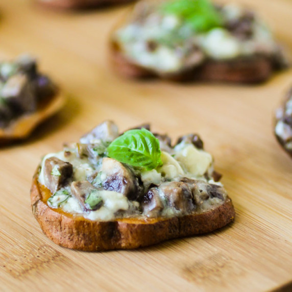 Close up shot of one sweet potato slice garnished with basil on a wooden cutting board with more in 