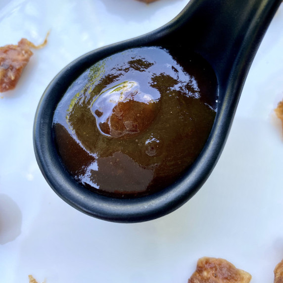 Tamarind sauce in a black sauce spoon with tamarind pulp scattered around.