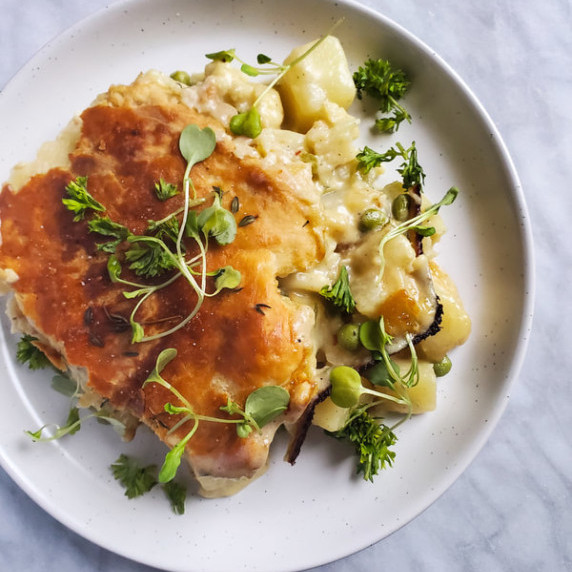 A golden brown crust on top of cheesy stew on a white plate against a white marble background