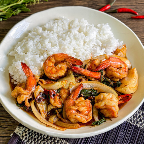 Close-up of spicy Thai basil shrimp with jasmine rice in a white dish.