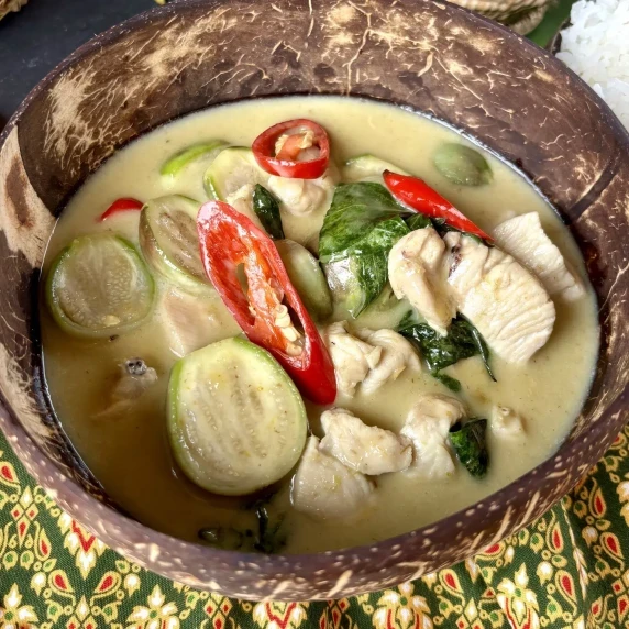 Thai eggplant green curry with chicken, chili, and sweet basil in a coconut bowl.