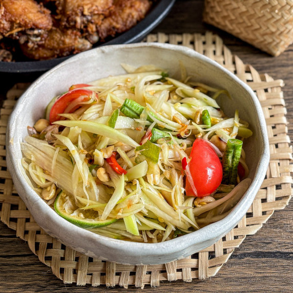 Close-up of Thai papaya salad with tomatoes, beans, and peanuts, in a white bowl.