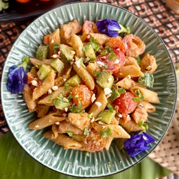 Thai peanut chicken pasta salad with tomatoes, penne, cucumbers, and peanuts.