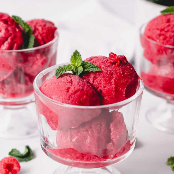 Three footed dessert bowls filled with ruby red raspberry sorbet garnished with fresh mint sprigs.