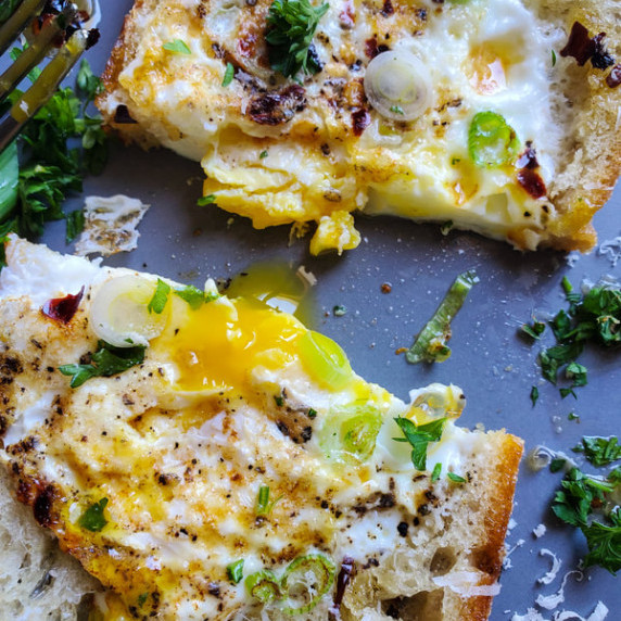 Runny yolk, fried egg, fried bread, fresh herbs, and spices, on a gray / blue plate.