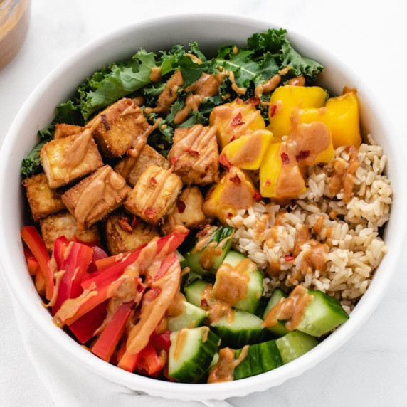 Bowl with baked tofu, mango, red bell pepper, cucumber, kale and brown rice.