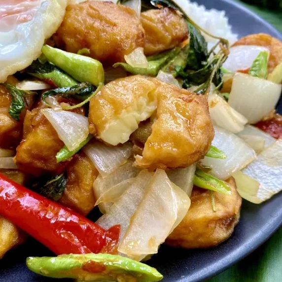 Stir-fried egg tofu with vegetables and Thai basil in a black dish.