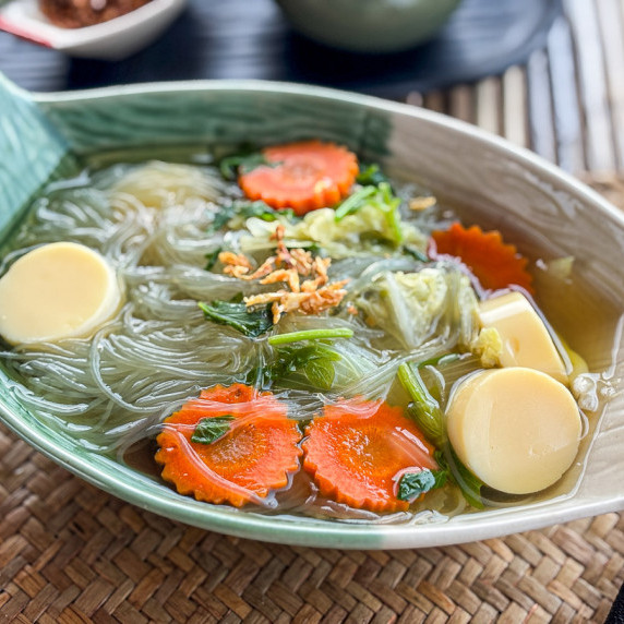 Thai tom jued soup served in a green leaf-shaped bowl with carrots, Chinese cabbage, and noodles.
