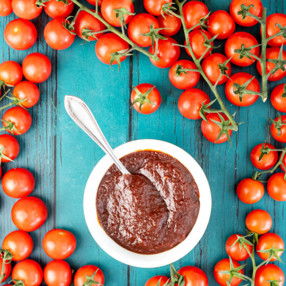 A bowl of ketchup surrounded by fresh tomatoes. 