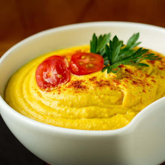 Close up side shot of hummus garnished with tomatoes, herbs, and paprika in a white bowl.