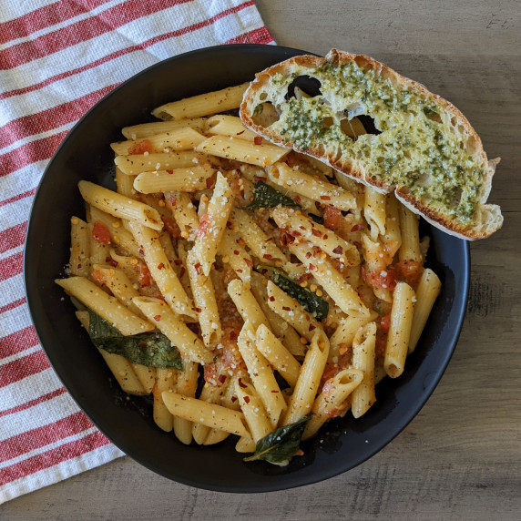 A bowl of penne pasta with tomatoes and basil served with a side of bread