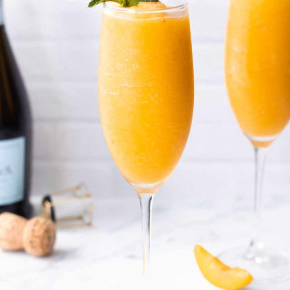 A frozen peach bellini cocktail in a champagne flute garnished with a mint sprig.