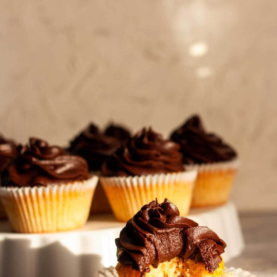 Vanilla cupcakes with chocolate frosting on a gray and white surface.