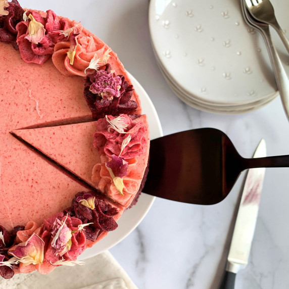 Top view of a slice of Vanilla Cake with Berry Buttercream being lifted with a black cake server.