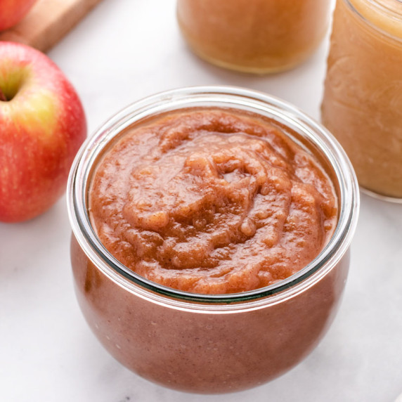 Homemade unsweetened applesauce in a glass jar with an apple.