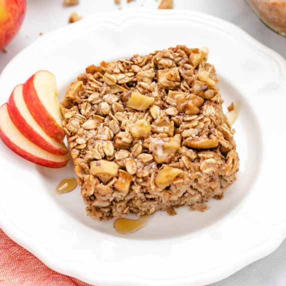 Vegan baked oats with apples cut into a square on a white plate with apple slices.