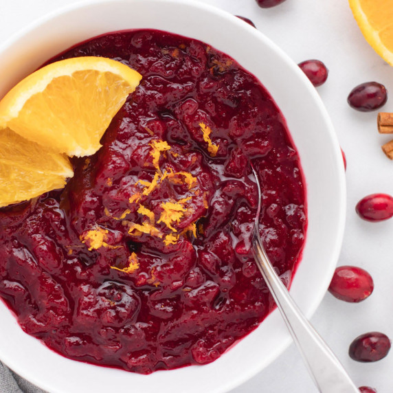 Vegan cranberry sauce in a bowl with orange slices and zest.