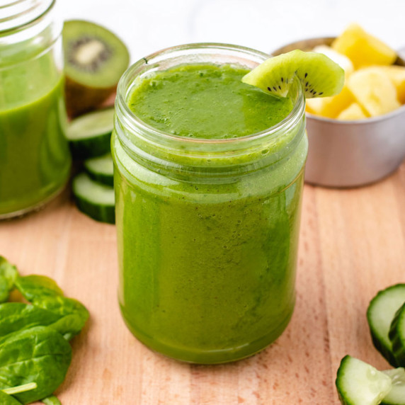 Pineapple cucumber smoothie in a glass jar with a wedge of kiwi.