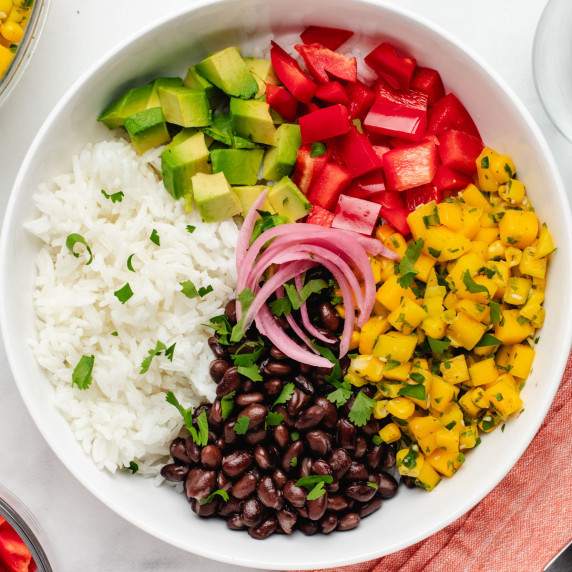 Rice, black beans, mango corn salsa, red bell pepper, avocado, and pickled red onions in a bowl.