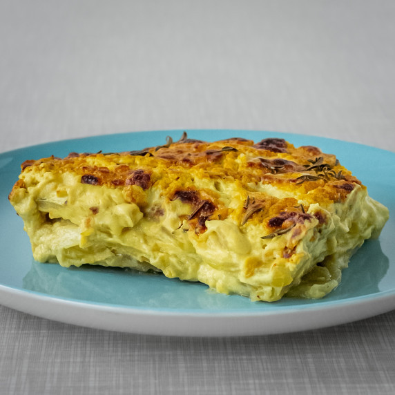 A turquoise plate on a grey table with creamy vegan dauphinoise potatoes