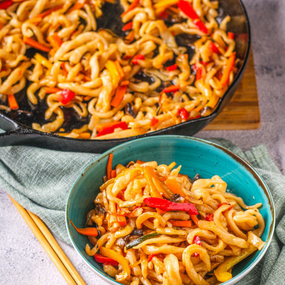 a bowl of stir fried udon noodles with vegetables in a spicy sauce.