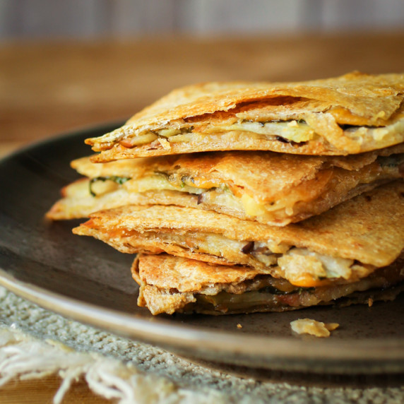 Crispy cheesy quartered quesadilla stacked on a brown plate placed on a beige napkin.