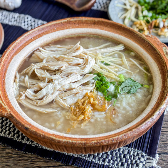 Close-up of khao tom gai with shredded chicken and fried garlic in a clay bowl.