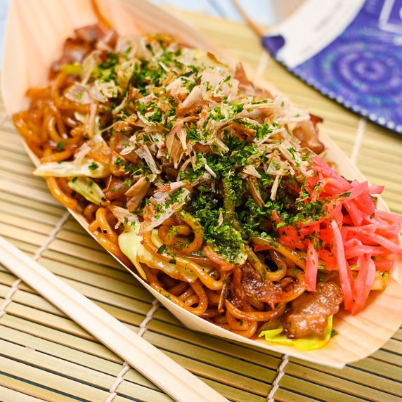 Yakisoba noodles arranged on a black plate on a blue wood effect surface