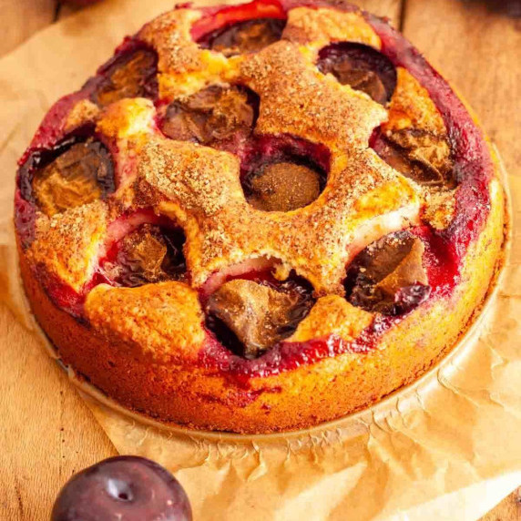 A yogurt plum cake on a wooden table next to plums.