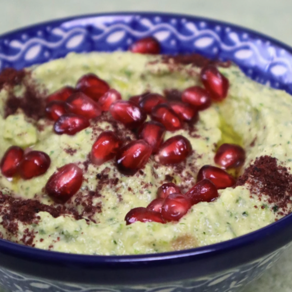 zucchini dip in a bowl topped with sumac and pomegranate seeds