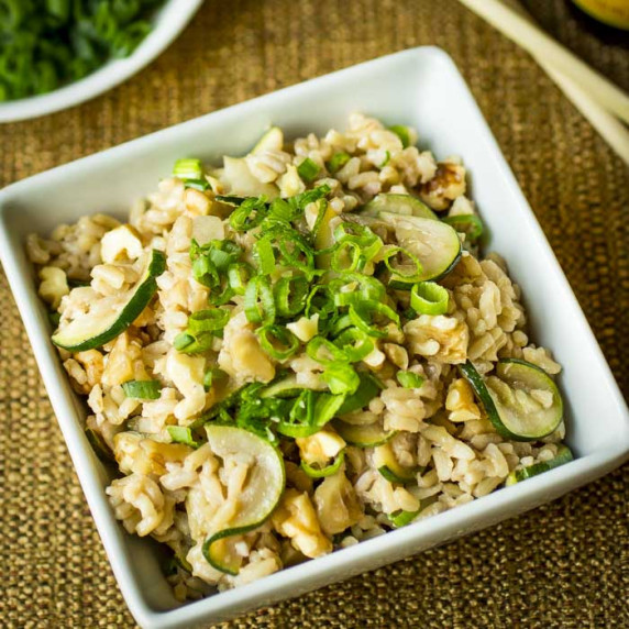 Overhead shot of a square white bowl with zucchini fried rice garnished with green onions.